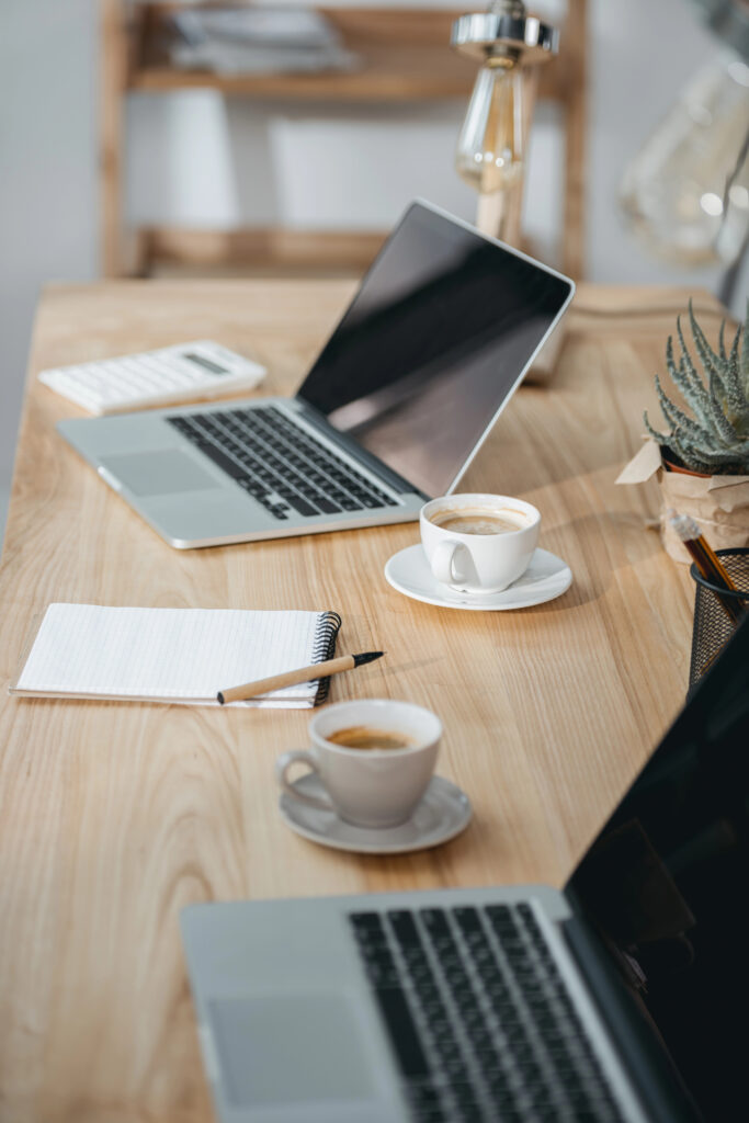 two lap top computers, two coffee cups, and a notepad on a desk